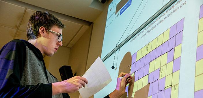 A BSU student at a white board dividing a grid into districts in a Math and Politics class